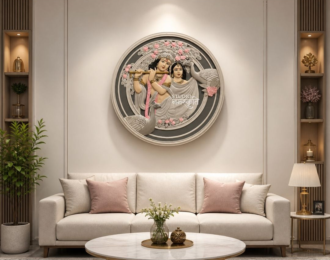 A framed circular wall art piece featuring a classical Indian painting of Radha Krishna, displayed in a modern living room setting above a light beige sofa. The image includes branding for  at the top and contact details at the bottom.